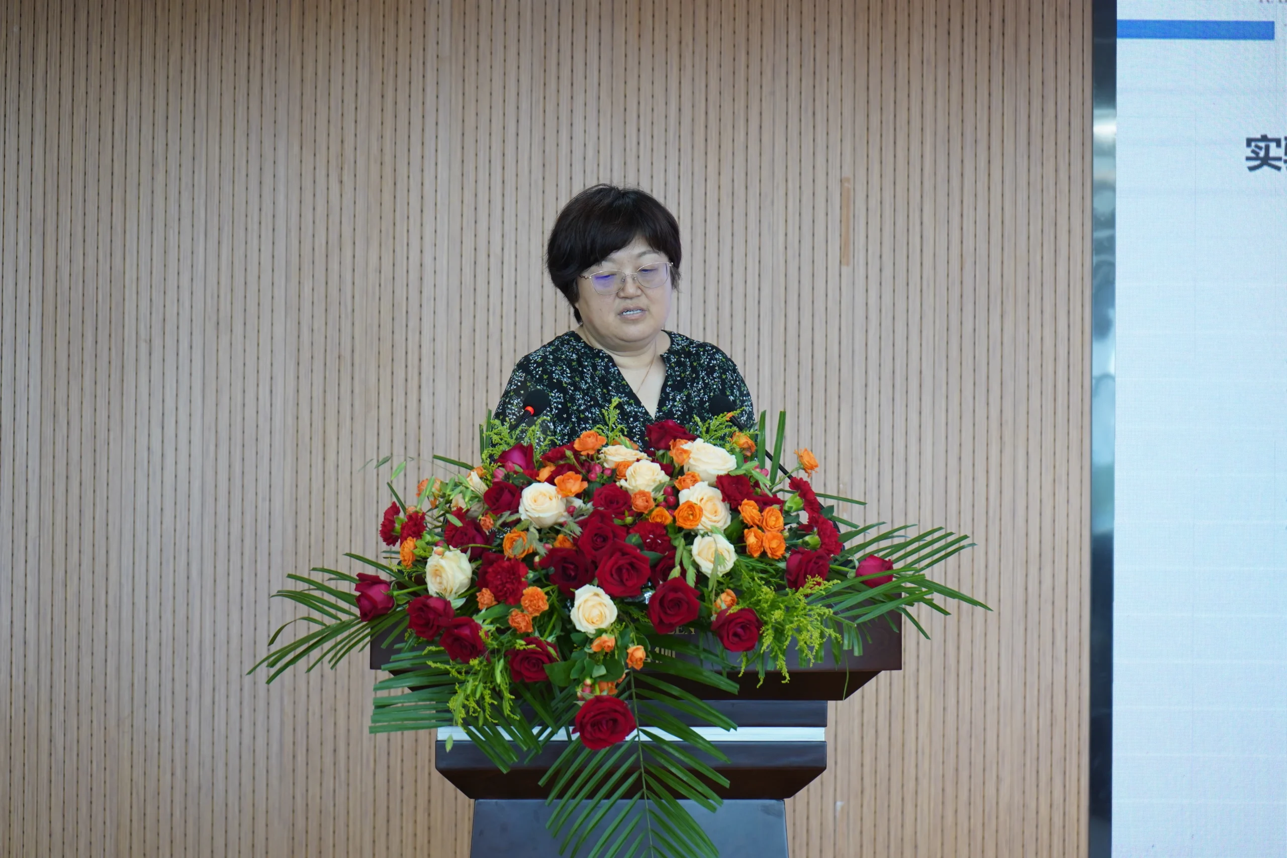 Industry representative giving keynote speech at corporate event with elegant flower display.